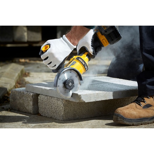 Person cuts concrete block with DEWALT angle grinder, wearing gloves and boots, dust visible.