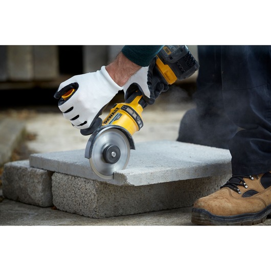 Person cuts concrete block with a DEWALT power tool, wearing gloves and work boots outdoors.