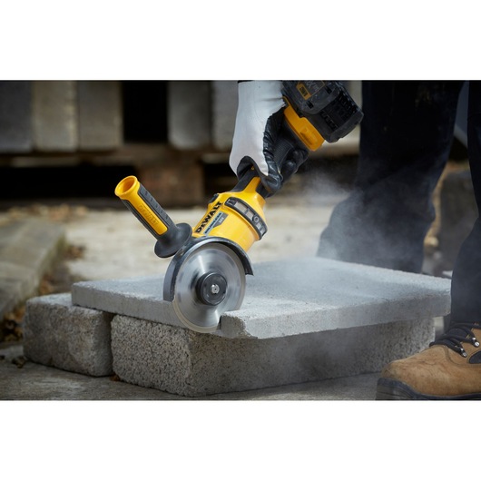 DEWALT DT3712 tool cutting concrete block outdoors, with dust and worker's gloved hand visible.