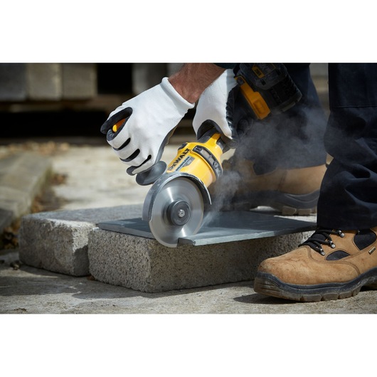 Person using a DEWALT angle grinder to cut stone outdoors, wearing gloves and safety boots.