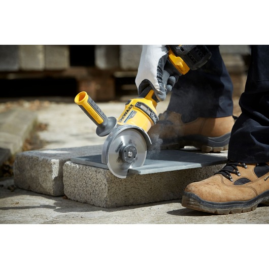 Person using DEWALT angle grinder to cut a stone slab outdoors, wearing gloves and safety footwear.
