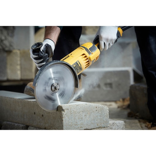 Person cutting a concrete block with a yellow DEWALT power tool, wearing gloves for safety.