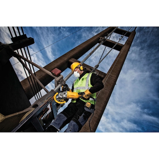 Worker in safety gear uses a DEWALT tool on a metal structure outdoors with blue sky in the background.
