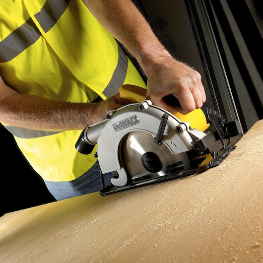 Person uses DEWALT circular saw to cut wood on workbench, wearing yellow safety vest.