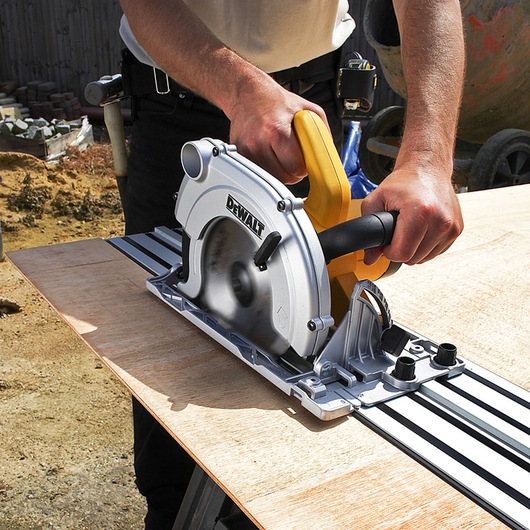 Person using a DEWALT circular saw to cut wood along a guide rail on a worktable outdoors.
