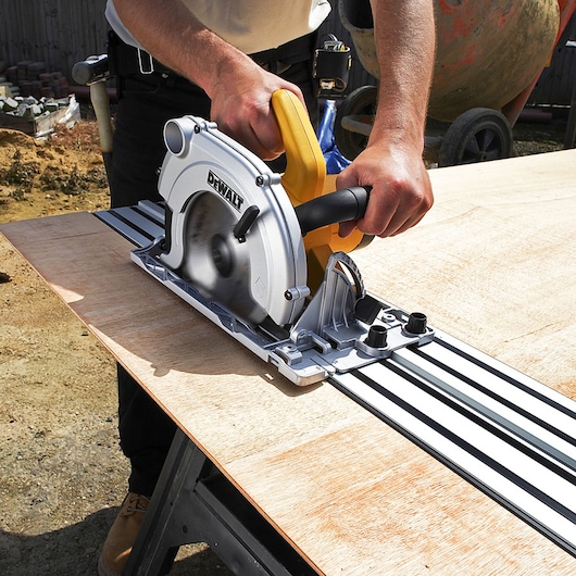 DEWALT circular saw cutting wood on a guide rail outdoors, held by a person.