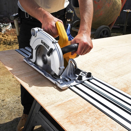 Person using a DEWALT circular saw with a track guide to cut a plywood sheet outdoors.