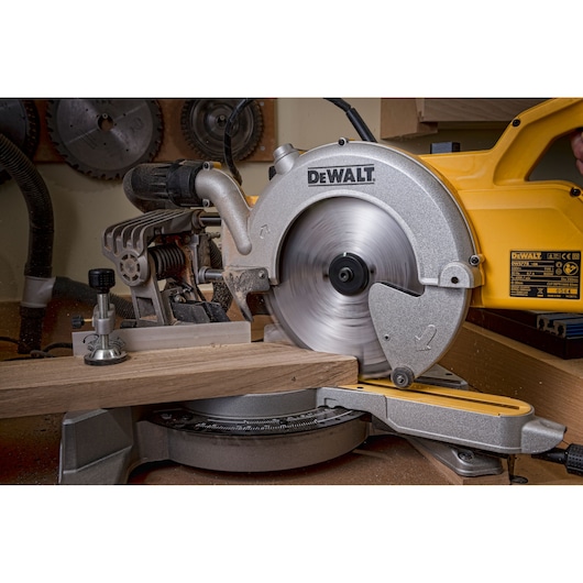 A DEWALT miter saw cutting a piece of wood in a workshop setting. The saw blade is spinning.