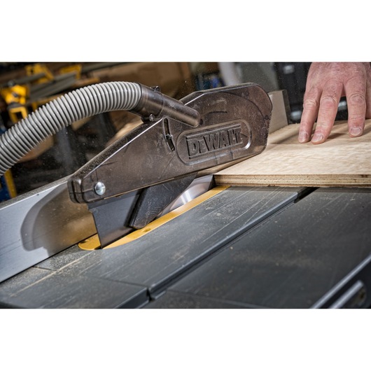 DEWALT table saw cutting wood, safety guard in place, close-up of hand and saw mechanism.