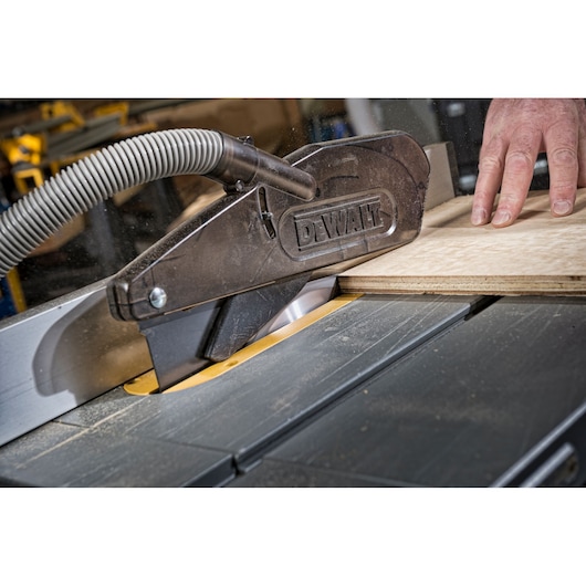 DEWALT table saw cutting wood with dust extraction hose and safety guard in use.