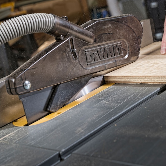 DEWALT table saw cutting wood, dust extraction hose attached for clean operation.