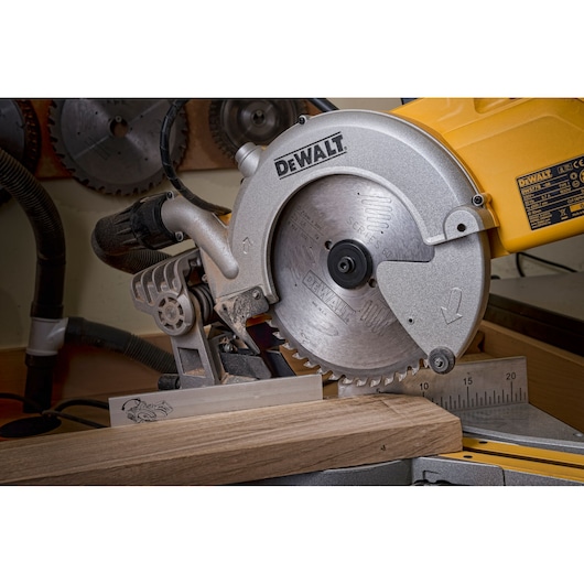 DEWALT circular saw cutting a wooden plank in a workshop, with measurement guide and other saw blades in the background.
