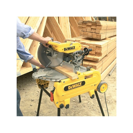 DEWALT miter saw cutting a wooden plank at a construction site with stacks of lumber in the background.