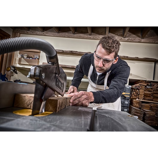 Person using a DEWALT table saw to cut wood in a workshop; wood pieces and tools are visible around.