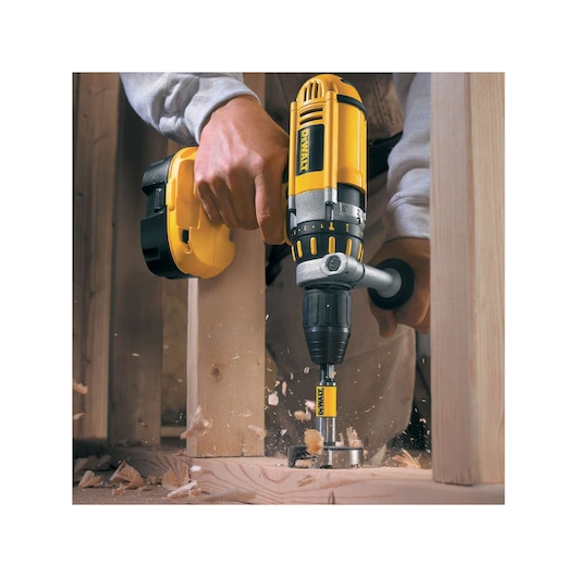 DEWALT drill is used to bore a hole in a wooden beam, wood shavings flying during the drilling process.