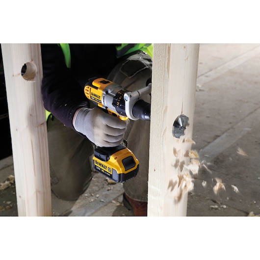 DEWALT cordless drill used to bore a hole in a wooden beam, wood chips flying during operation.