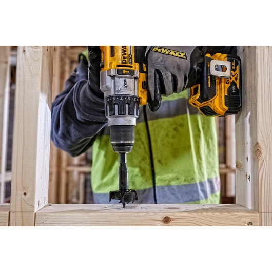 DEWALT cordless drill used to drill a hole in a wooden frame at a construction site. Close-up view of tool in action.