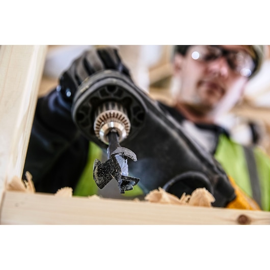 Close-up of DEWALT DT4585 drill bit in use, drilling through wood with visible shavings and gloved hand.