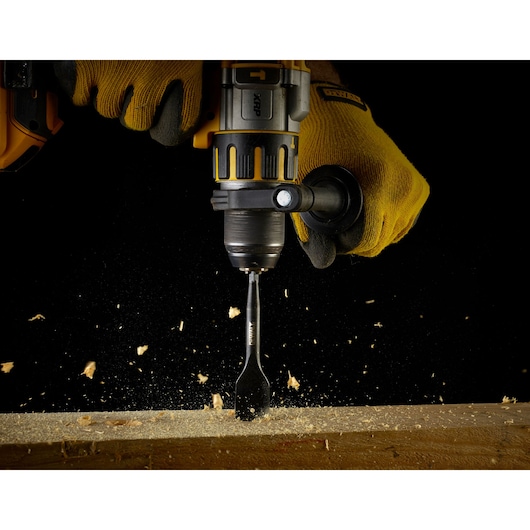 DEWALT power drill in use, drilling a hole in wood with wood chips flying, operator wearing yellow gloves.