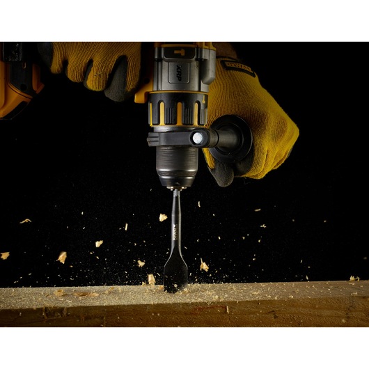 DEWALT drill with spade bit drilling wood, worker wearing yellow gloves, wood chips flying.