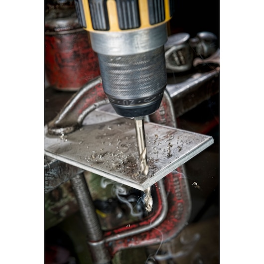 DEWALT drill with metal drill bit making a hole in a metal sheet held by a clamp, metal shavings visible.