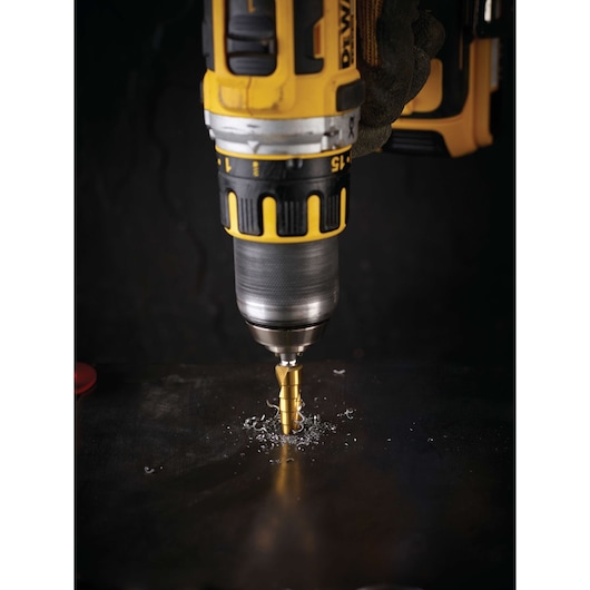 DEWALT drill with a step drill bit in use, drilling through a metal surface with metal shavings around the bit.