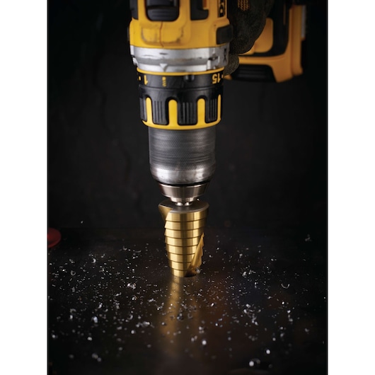 Close-up of a DEWALT drill with step drill bit cutting through a metal surface, surrounded by metal shavings.