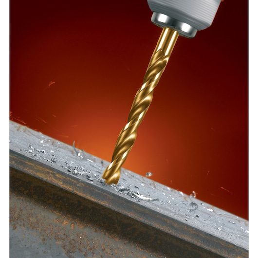 A close-up of a golden drill bit attached to a power drill, drilling into a metal surface with metal shavings and sparks visible.