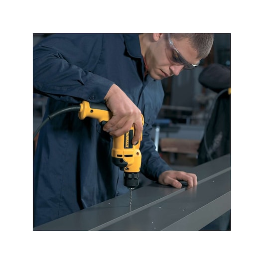 Person drilling metal with a yellow DEWALT electric drill in a workshop.