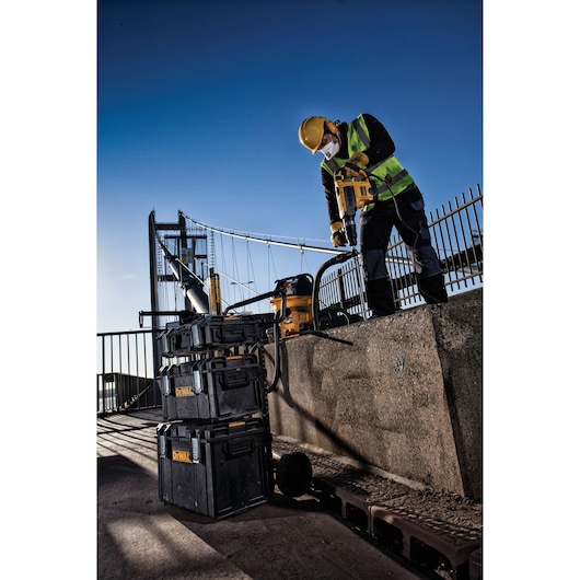 Worker uses DEWALT tools and storage boxes outdoors on a bridge construction site, wearing safety gear.