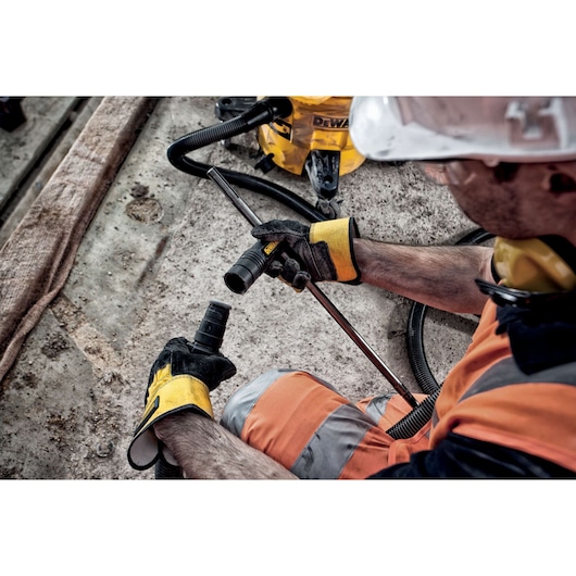 Worker in safety gear connects DEWALT vacuum hose on a construction site with concrete floor.