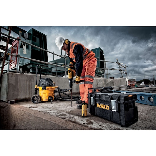 DEWALT toolcase and drill in use at a construction site. Worker in safety gear operates equipment outdoors.