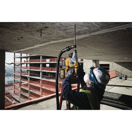 Worker uses DEWALT drill with dust extractor to drill into a concrete ceiling at a construction site.