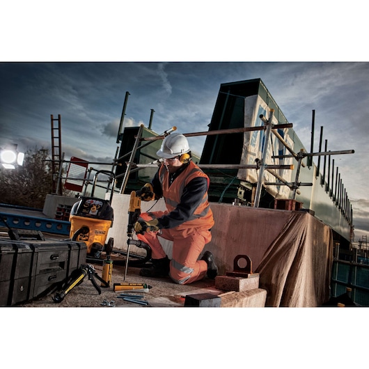 Worker using DEWALT drill on a construction site, wearing safety gear and surrounded by DEWALT tools and equipment.