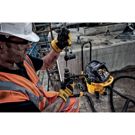 Worker uses DEWALT DT60340 drill and equipment at construction site, wearing gloves and safety vest.