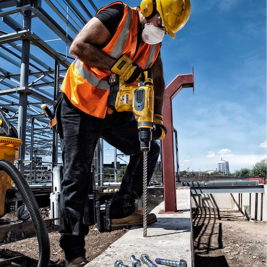 DEWALT DT60814, DT60814-QZ drill bit in use at construction site. Worker drills concrete with yellow power tool.