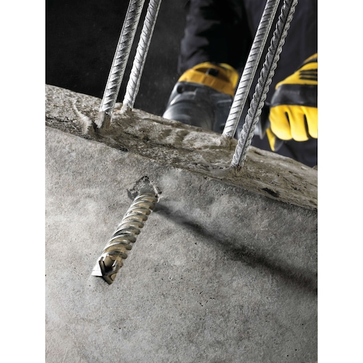 Close-up of a DEWALT drill bit boring into concrete with metal rebar and gloved hands visible.