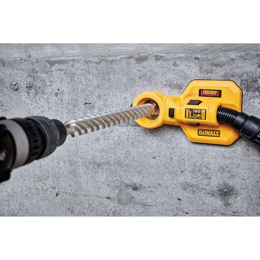 DEWALT tool attachment used on concrete wall with a drill and vacuum hose for dust extraction.