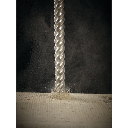 Close-up of a spiral drill bit making a hole in concrete, with dust visible around the tip.