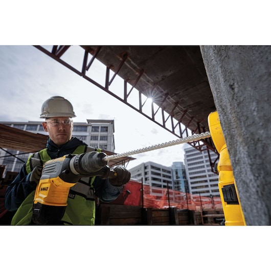 Worker uses a DEWALT drill on a construction site with buildings in the background.
