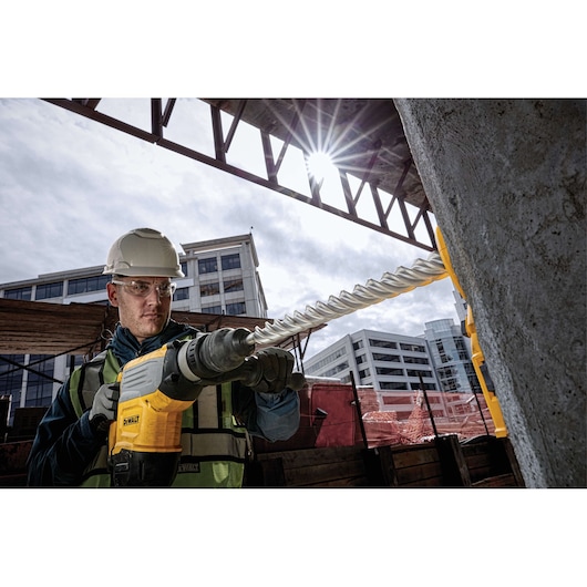 Worker using DEWALT rotary hammer drill with DT60845 bit on concrete at construction site.
