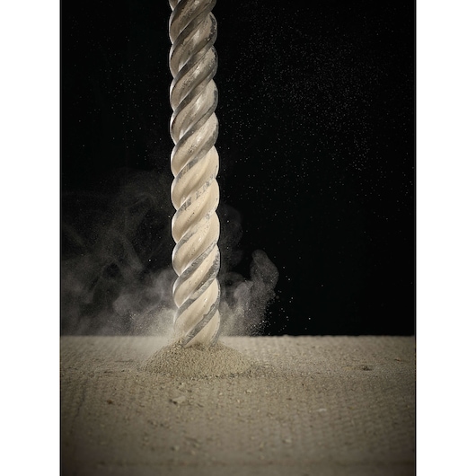 Close-up of a DEWALT drill bit boring into concrete, creating dust and debris against a dark background.