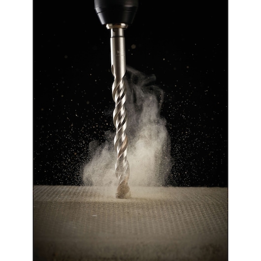 A close-up of a DEWALT drill bit in action, drilling into a concrete surface with dust rising around the bit.