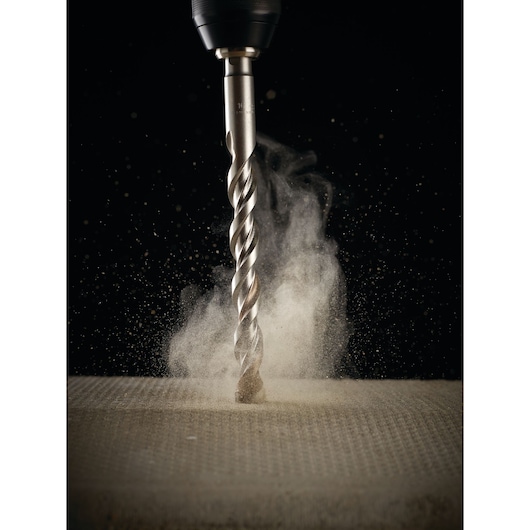 A close-up image of a DEWALT DT6686 drill bit in action, drilling into a concrete surface with dust and particles flying around, set against a black background.
