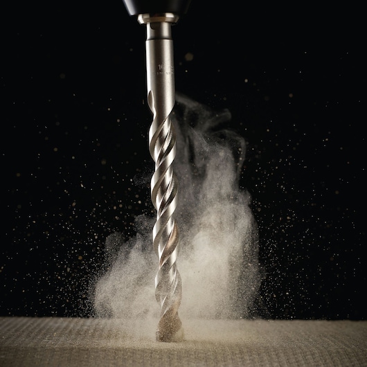 Close-up of a DEWALT drill bit creating dust as it drills into a surface against a dark background.