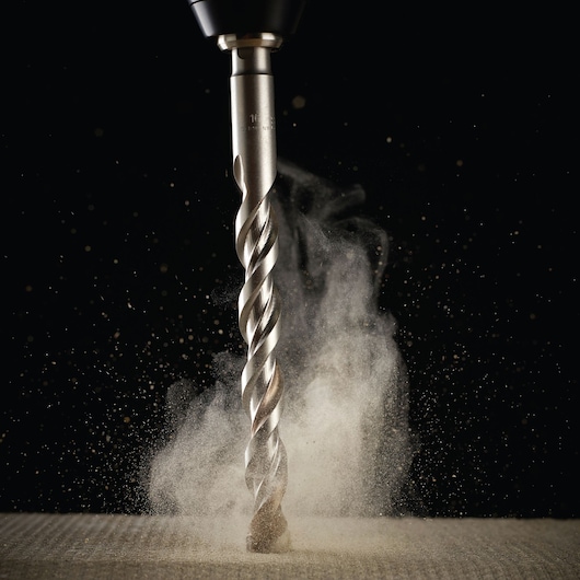 Close-up of a DEWALT drill bit cutting material, with dust particles rising on a dark background.
