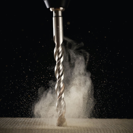 Close-up of a DEWALT drill bit cutting into material, dust rising around the sharp metal spiral.