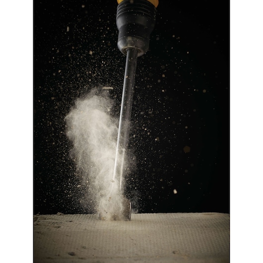 Chisel striking concrete, dust scattering on impact, close-up against dark background.