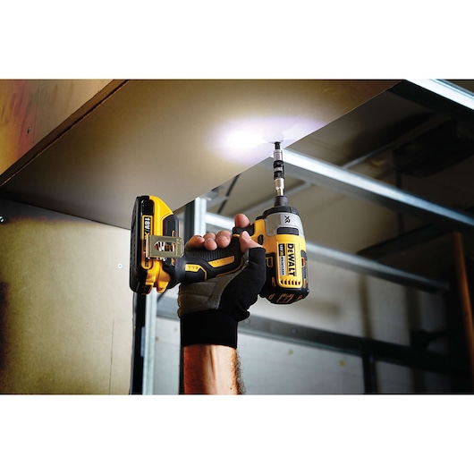 Person using a DEWALT cordless drill to drive a screw into a ceiling panel in an indoor construction setting.