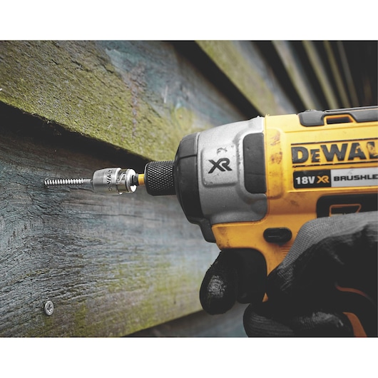 DEWALT cordless drill driving a screw into wood siding, close-up of tool and gloved hand.